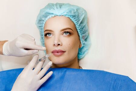 Lips augmentation injections for attractive girl. Plastic surgeon does injection in lip in medical clinic. Cosmetic rejuvenating facial treatment. Empty space for advertの写真素材