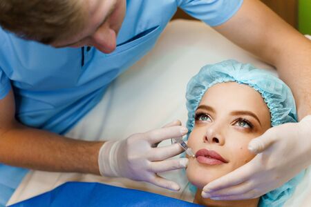 Closeup lips augmentation injections for attractive girl. Plastic surgeon does injection in lip in medical clinic. Cosmetic rejuvenating facial treatment. Empty space for advertの写真素材