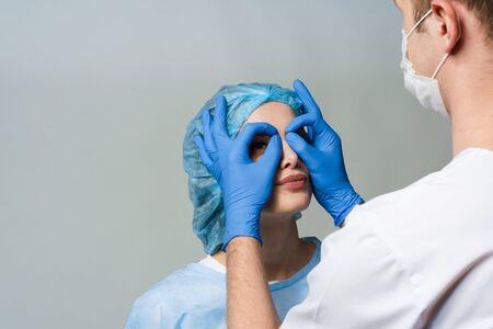 Funny consultation with jokes of plastic surgeon in medical center. Doctor man in mask asks girl patient about injections on the lips, chin, forehead. Wrinkle removalの写真素材