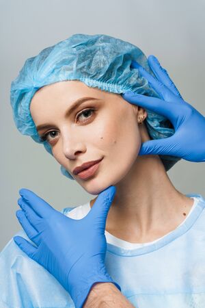 Closeup consultation with plastic surgeon on white background. Cosmetic rejuvenating facial treatment. Doctor man with blue medical gloves touches girl face. Patient ask about lips and chin injectionsの写真素材
