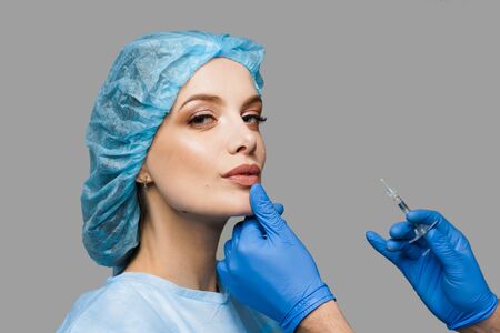 Lips augmentation injections for attractive girl on white background. Plastic surgeon does injection in lip in medical clinic. Cosmetic rejuvenating facial treatment. Empty space for advertの写真素材