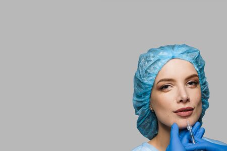 Lips augmentation injections in underlip for attractive girl on white background. Plastic surgeon does injection in lip. Cosmetic rejuvenating facial treatment. Empty space for advertの写真素材