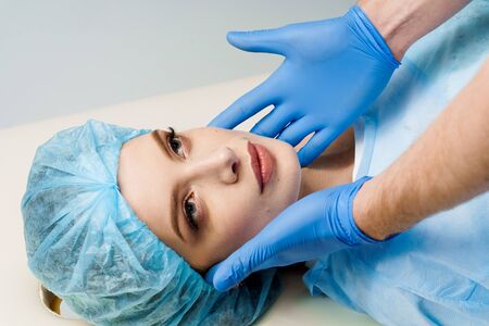 ?onsultation with plastic surgeon on white background. Cosmetic rejuvenating facial treatment. Doctor man in mask asks girl patient about injections on the lips, chin, forehead. Wrinkle removalの写真素材