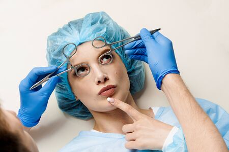 Funny consultation with jokes of plastic surgeon in medical center. Doctor man in mask asks girl patient about injections on the lips, chin, forehead. Wrinkle removalの写真素材