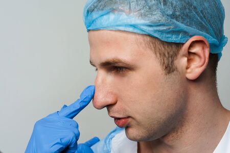 Facebuilding. Septoplasty and nose rhinoplasty. Doctor touches man nose on consultation. Inspection before plastic surgery. Cosmetic rejuvenating facial treatment. Nasal septum curvature correctionの写真素材