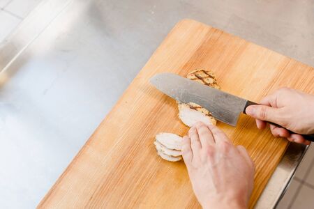 Raw fillet of chicken on cutting board. Cut fillet for ramen soup on kitchen . Chef cooks meat with...