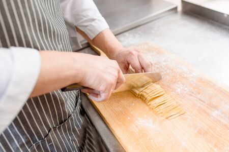 Cut noodles on kitchen . Chef cooks spaghetti in restaurant. Chef cuts with a knife raw noodles with flourの写真素材