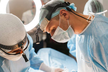 Surgeon with headlamp and scissors do plastic operation in medical clinic. Chest augmentation plastic operation and correction in medical clinicの写真素材