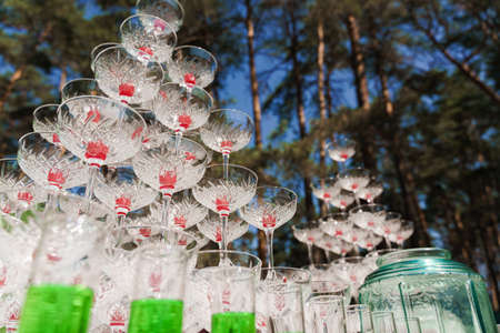 Drink coctkail catering for wedding. Big pyramid of glasses with champagne and red cherry inside on business meeting at summer day in the forest.の写真素材