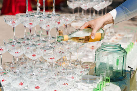 The waiter pours champagne into crystal glasses close up. Sparkling wine pouring in wine glass at summer day. Catering for business peopleの写真素材