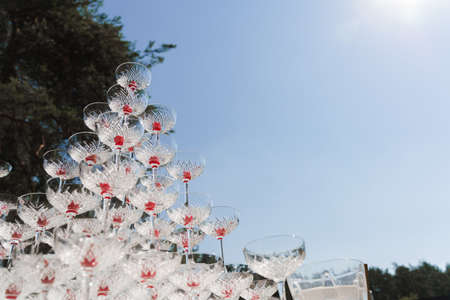 Pyramid of glasses with champagne and red cherry inside on business meeting at summer day. Alcohol cocktails for guests. Business meeting open air with social distancingの写真素材