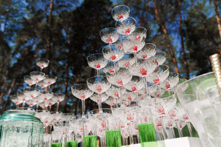 Shot glasses with green syrup near big pyramid of glasses with champagne and red cherry inside on business meeting at summer day in the forestの写真素材