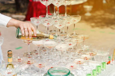 The waiter pours champagne into crystal glasses close up. Sparkling wine pouring in wine glass at summer day. Catering for business peopleの写真素材