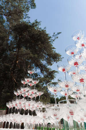Pyramid of glasses with champagne and red cherry inside on business meeting at summer day. Alcohol...