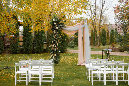 Wedding decoration of marriage ceremony in autumn. White chairs and wedding arch for couple in the forestの写真素材