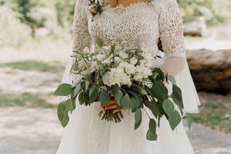 Wedding bouquet with white roses and green leaves. Bride in dress holds bouquet. Advert for wedding agency.の写真素材