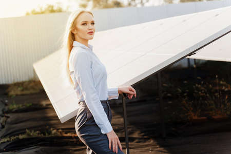 Girl stand near solar panels row on the ground with sun light. Woman investor wears formal white shirt. Free electricity for home. Sustainability of planet. Green energy.の写真素材