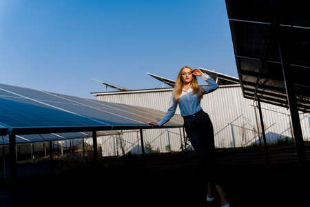 Girl walks between 2 Solar panels row on the ground at sunset. Woman investor wears formal white...