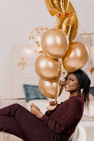 Muslim black girl with golden helium balloons smiles. African young woman celebrates her birthdayの写真素材