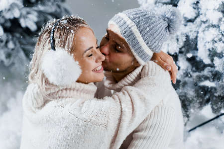Winter love story with couple weared fur headphones, hats, white sweaters. Happy young couple hugs...
