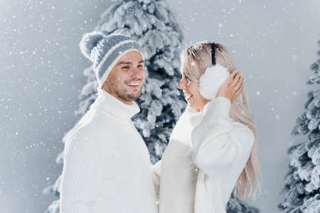 Winter love story with couple weared fur headphones, hats, white sweaters. Happy young couple hugs...