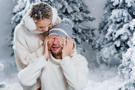Couple seat on the snow and hug, kiss, and have fun each other. Winter love story before new year celebration. Waiting for christmas gift. Happy couple weared fur headphones, hats, white sweaters.の写真素材