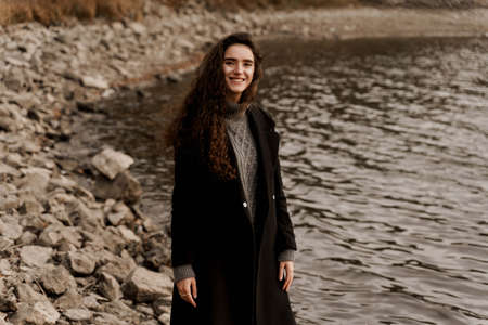Young woman with curly hair looks at the lake and dreams about her life.