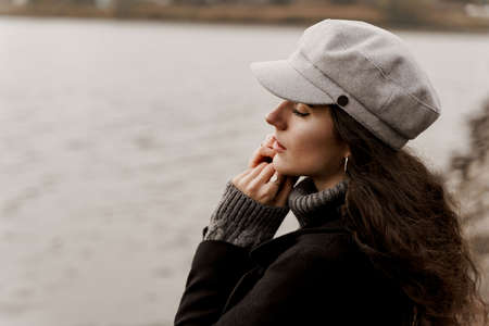 Beautiful girl in a black coat and a gray woolen cap near the lake. Traveling in your countryの写真素材