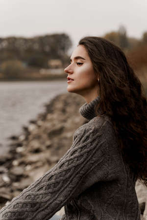Girl with curly hair on the background of birch with stones and lake in autumn