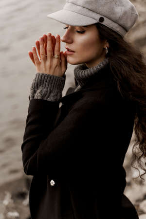 A beautiful girl close-up in a black coat and a gray woolen cap near the lake. Traveling in your countryの写真素材