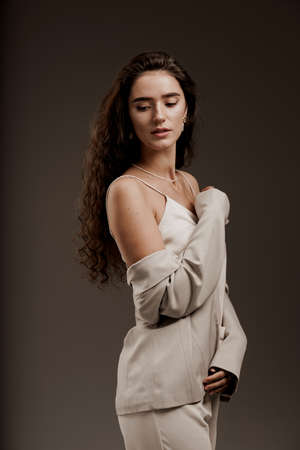 Fashion, elegant and sexy professional model in studio. Gorgeous young female in classic suit in photostudio. Attractive girl with curly hair posing for commercial photoshootの写真素材