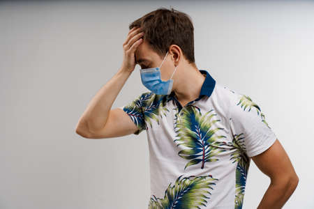 Headache man in blue medical mask isolated white background. Man touches her head because sicks...