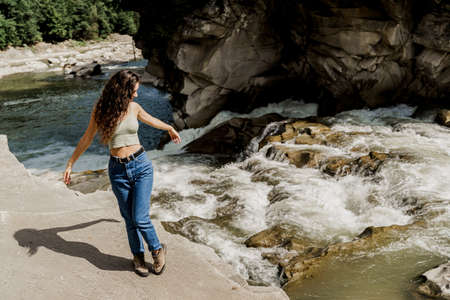Girl is traveling in Karpathian mountains and feeling freedom. Waterfall in mountain river. Cascade...