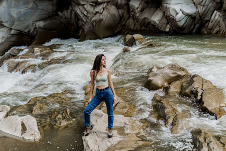 Girl is traveling in Karpathian mountains and feeling freedom. Waterfall in mountain river. Cascade waterfall and beautiful young womanの写真素材