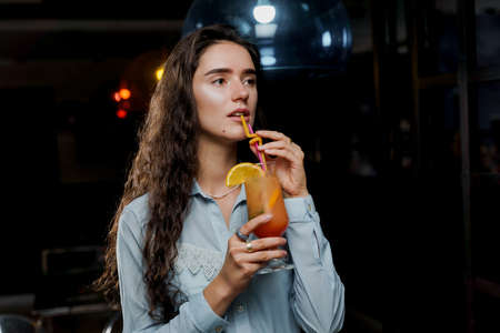 Girl with cocktail is drinking in night club before party. Advert for bar and night clubs. Citrus alcohol drink with orange juiceの写真素材