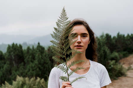 Girl is holding leaf of fern and traveling in the mountains. Foggy day. Hiking and climbing up to the peak of the mountain. Beautiful nature of Ukraine.の写真素材