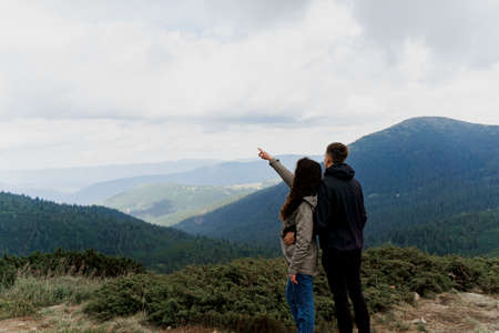 Couple at the peak of the mountain. Girl is pointing to the sky. Lifestyle of traveling people. Love story in the mountainsの写真素材