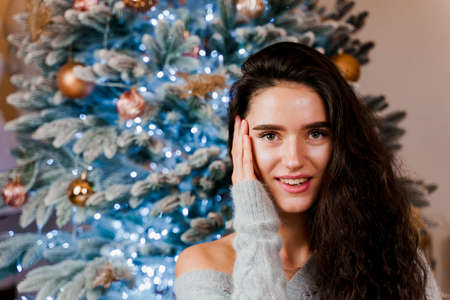 Girl near the Christmas tree smiling and posing. Seasonal advertising before the new year....