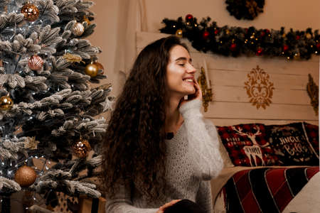 Girl near the Christmas tree smiling and posing. Seasonal advertising before the new year....