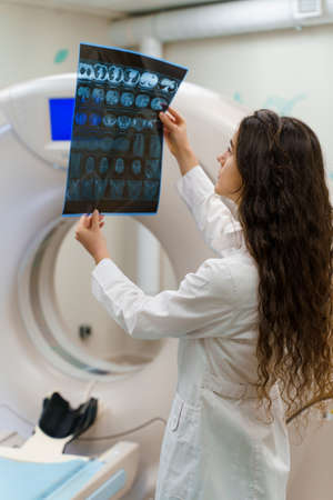 Vertical picture of medical student who looks at x-ray picture of patient brain near kt komputer tomograhphy. Young girl in medical clinic gotes new expirienceの写真素材