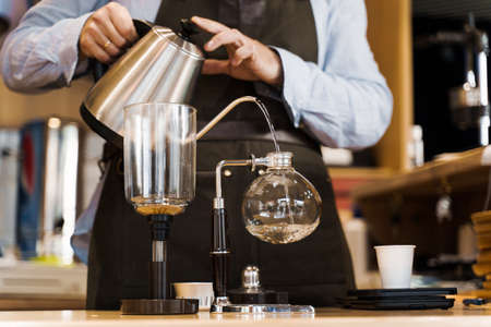 Syphon alternative method of making coffee. Barista pours hot boiling water in syphon device for coffee brewing in cafe. Scandinavian method of coffee making.の写真素材
