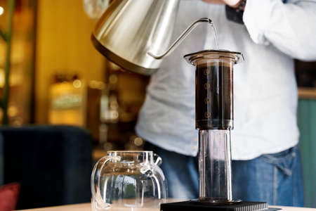 Aeropress coffee close up alternative making by barista in the cafe. Scandinavian coffee brewing method. Barista pours water to aeropress with coffee using kattle. Advert for cafe, restaurants.の写真素材