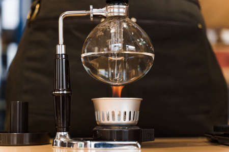Syphon coffee close-up device with fire heats glass flask in cafe. Alternative coffee brewing method. Creative idea for advert in cafe. Professional device for coffee.の写真素材
