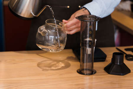 Aeropress coffee alternative making by barista in the cafe. Barista pours hot water in pot for making aeropress coffee with special device. Advert for cafe, restaurants.の写真素材