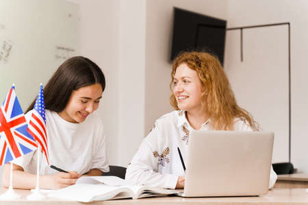 Foreign school private study with a school girl. Teacher explain grammar of native language using laptop. Prepearing to exam with tutor. English and British flags in front.の写真素材