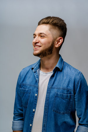 Young handsome man stands over white background and touches smiles after visiting barbershop. Confident man wears casual jeans shirt and looks in camera. Bearded caucasian business man.の写真素材