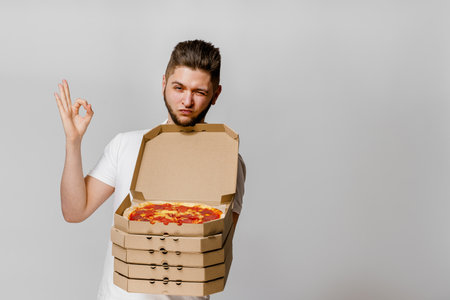 Young caucasian man shows that OK. On-line pizza delivery from restaurant. Safety delivery without coronavirus. Advertise for pizzeria. Stay at home and eat a pizza.の写真素材