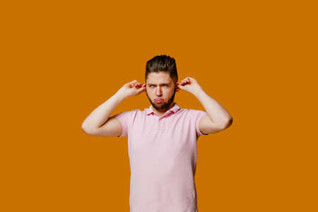 Funny handsome man fools around and makes crazy emotions. Caucasian man wears pink t-shirt. Isolated orange backround. Online work at home quarantine conceptの写真素材
