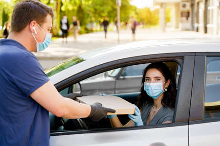 Safe food delivery from pizzeria to car during quarantine coronavirus. Attractive business woman in...