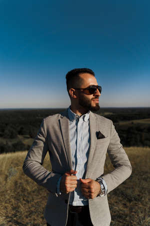 Handsome bearded arabian man in sunglasses on the blue sky background. Confident muslim business man. Arab man weared in gray coatの写真素材